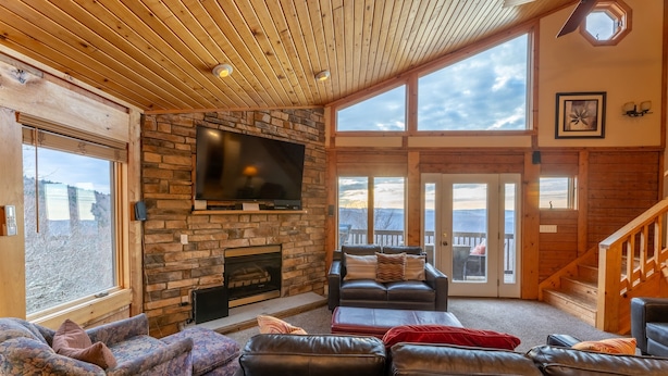 Una sala de estar acogedora con chimenea de piedra, sofás de cuero y un televisor grande.