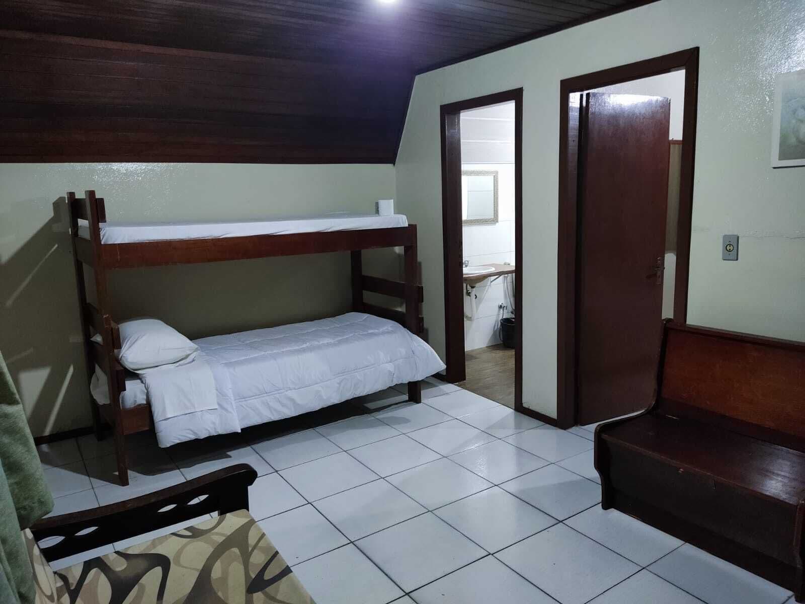 Dormitorio con literas, techo de madera, suelo de baldosas y un banco.