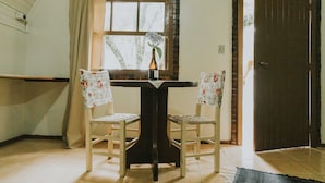 A room with a wooden table and two chairs, a window with curtains, and a door. - Villa Chalés Gramado - OH HOTEIS (Gramado)