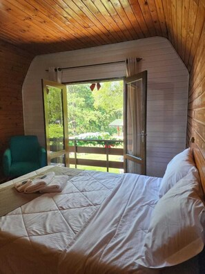 A cozy cabin room with a bed, a green chair, and a large window with an open door. - Villa Chalés Gramado - OH HOTEIS (Gramado)