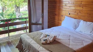 A bedroom with a wooden ceiling, a large bed with white linens, a wooden floor, and a sliding glass door leading to a balcony with a view of trees. - Villa Chalés Gramado - OH HOTEIS (Gramado)