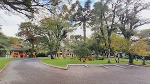 A pathway leading to a building with a green roof, surrounded by trees and a well-maintained lawn. - Villa Chalés Gramado - OH HOTEIS (Gramado)