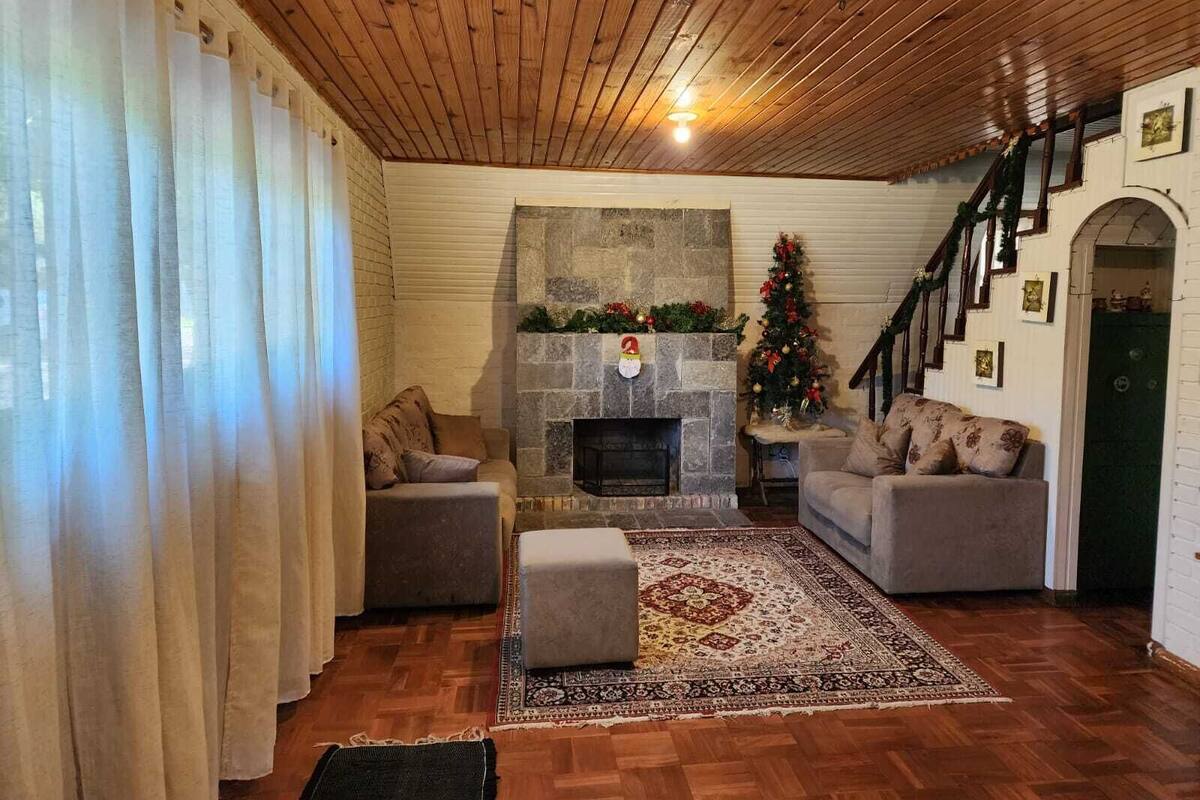 Un salon chaleureux avec une cheminée en pierre, deux canapés, un tapis et un escalier menant à un niveau supérieur.