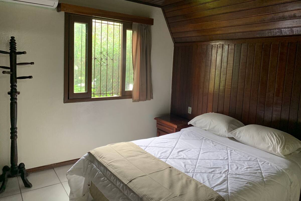 Une chambre avec un plafond en bois, un lit avec une literie blanche, une fenêtre avec des rideaux et une table de chevet en bois.