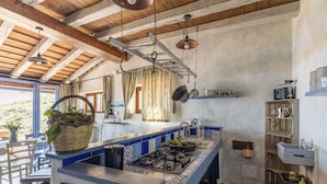 Una cocina rústica con estufa a gas, ollas colgantes y techo de madera.