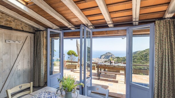 Una habitación con techo de madera, una mesa con sillas y vistas a un pueblo costero a través de amplios ventanales.