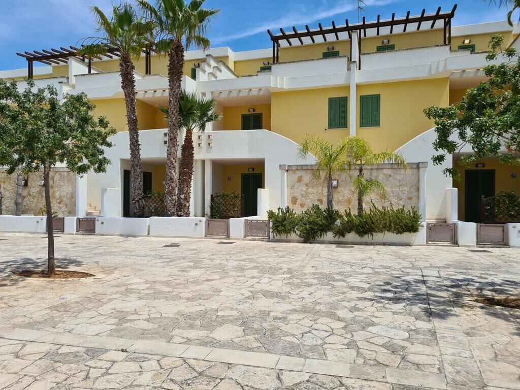 Un cortile con pavimento in pietra, palme e un edificio con balconi e persiane verdi.