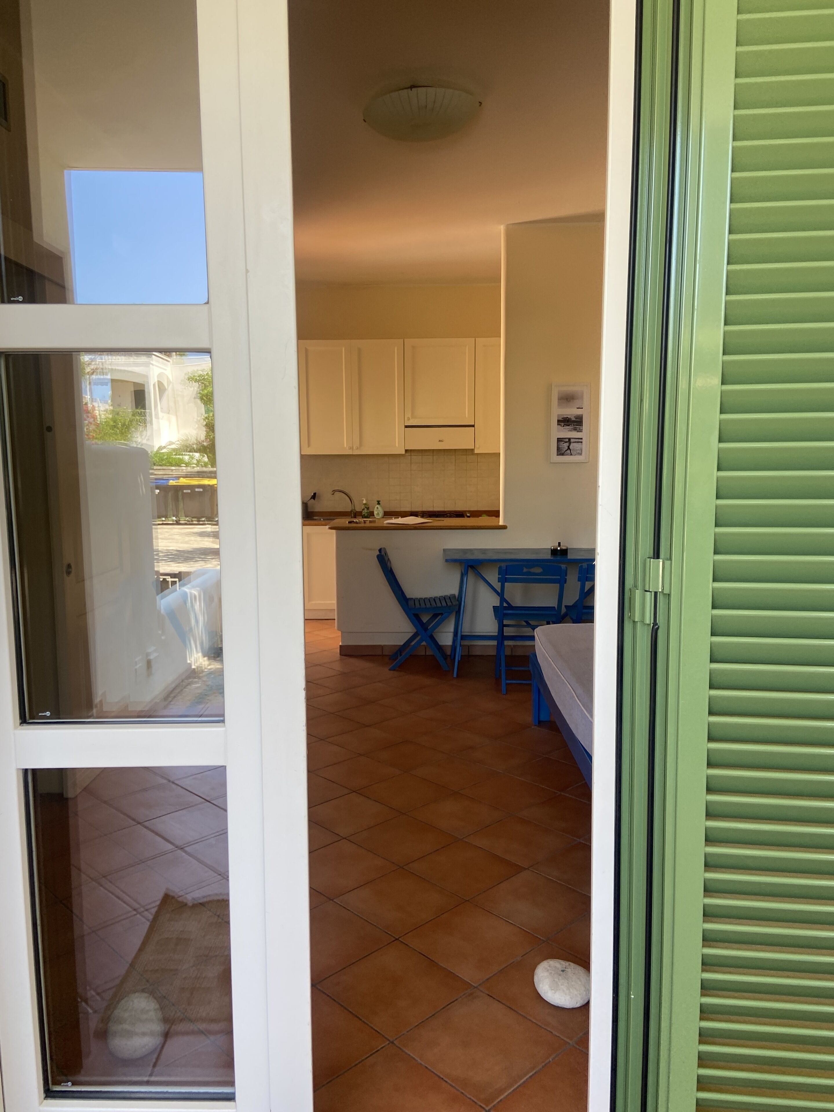 Una cucina con mobili bianchi, un tavolo blu e una finestra con vista su un giardino.