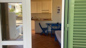 Une cuisine avec des meubles blancs, une table bleue et une fenêtre donnant sur un jardin.