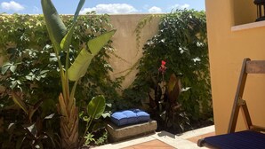 Un espace extérieur aménagé en patio, avec un sol carrelé, un banc bleu doté de coussins et diverses plantes.