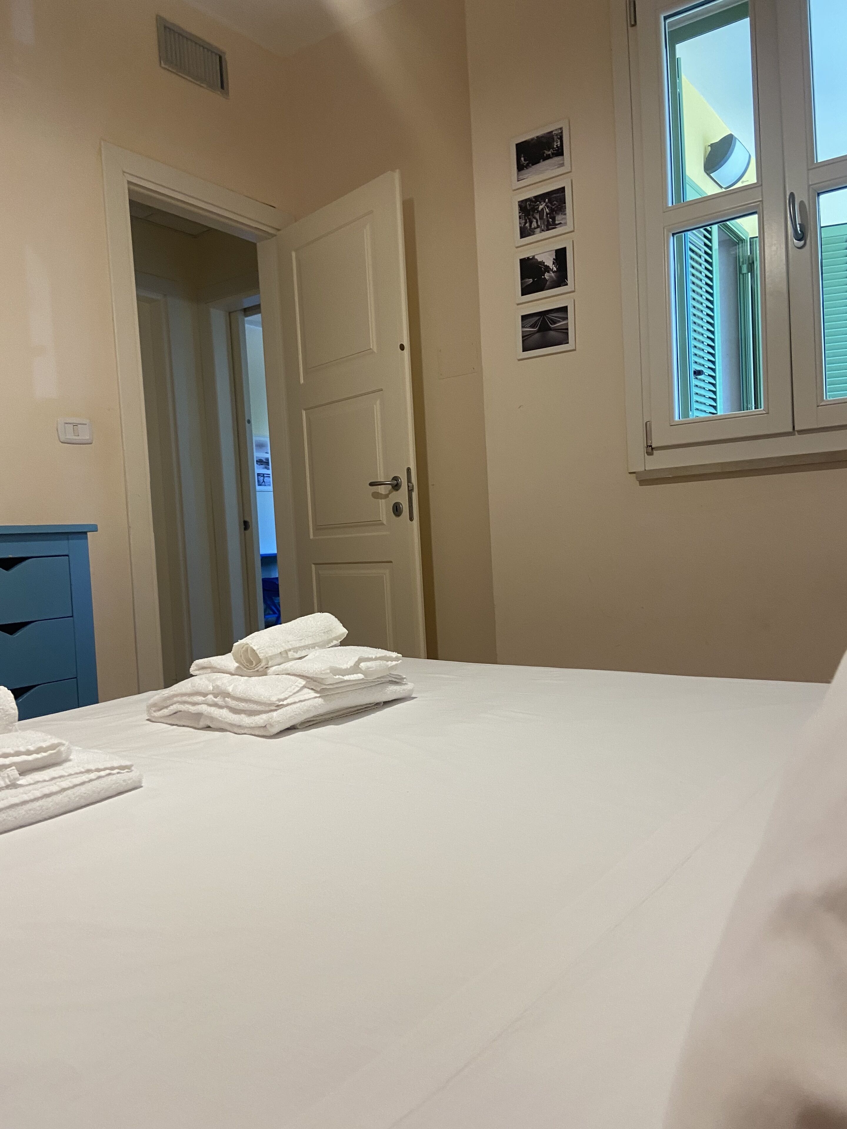 Una camera d'albergo con un letto, una porta, una finestra con persiane e un quadro appeso al muro.