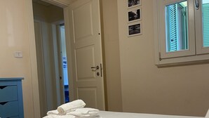 Une chambre d’hôtel avec un lit, une porte, une fenêtre avec des stores et un tableau accroché au mur.