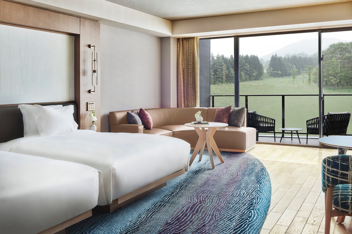 A hotel room with a large bed, a sofa, a small table, and a balcony with chairs.