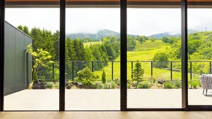 A spacious balcony with a wooden floor, large glass doors, and a view of a green landscape with trees and hills. - Intercontinental Appi Kogen Resort by IHG (Hachimantai)