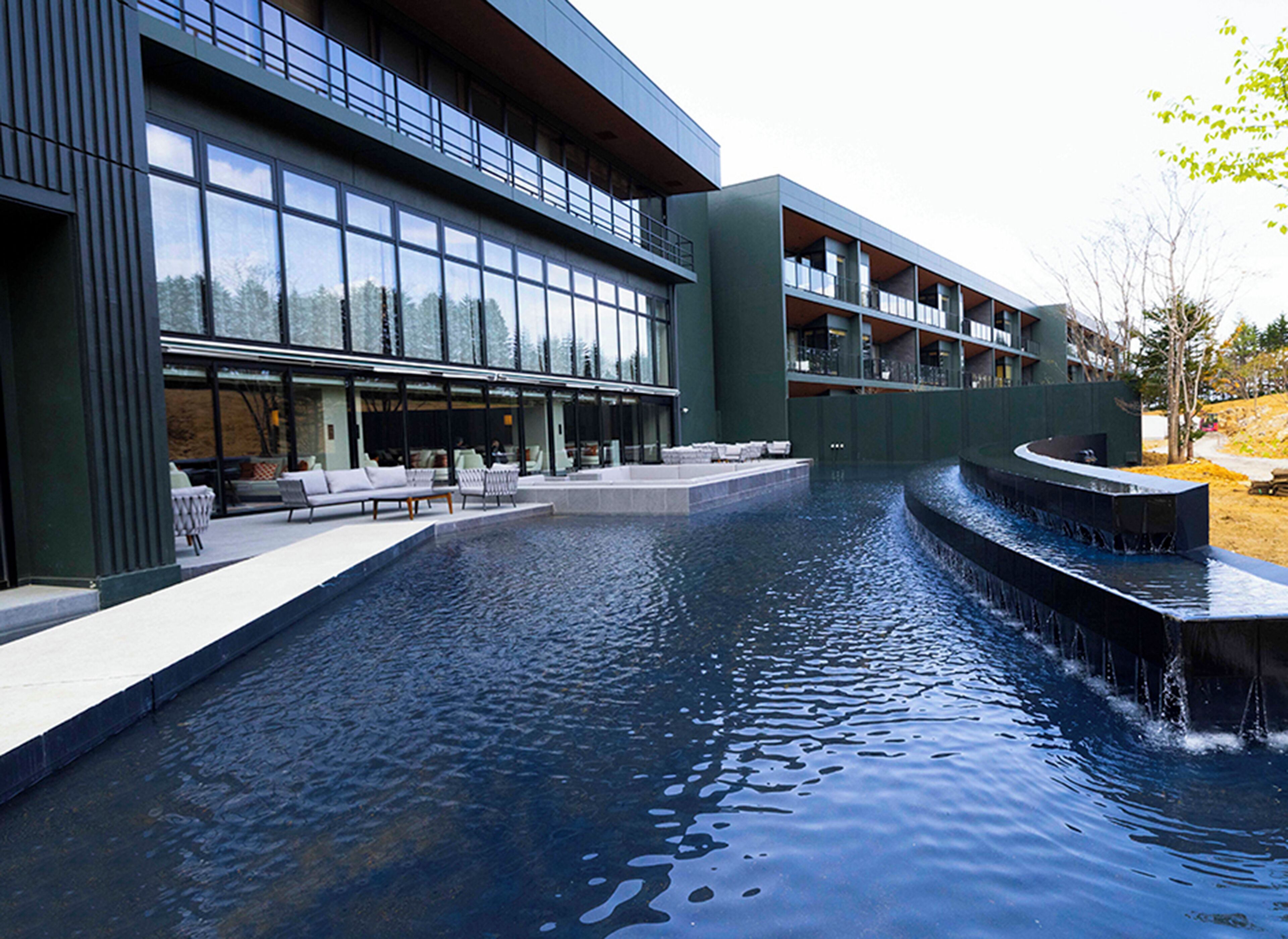 A modern building with a large pool, outdoor seating, and a waterfall feature.