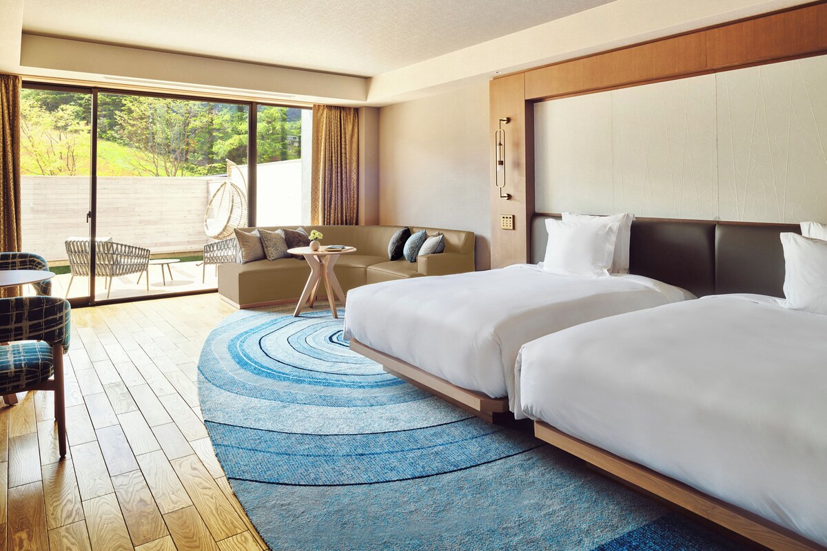 A hotel room with two beds, a sofa, a small table, and a chair.