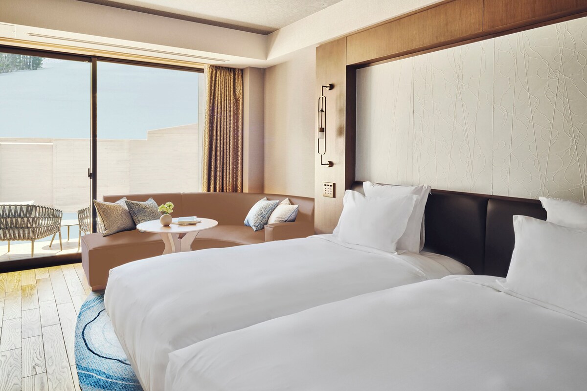 A hotel room with a large bed, a sofa, a small table, and a balcony with outdoor seating.