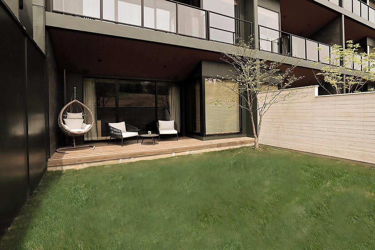 A modern outdoor patio with a hanging chair, two sofas, and a small table.