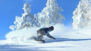 A snowboarder carving through deep snow with a clear blue sky in the background.