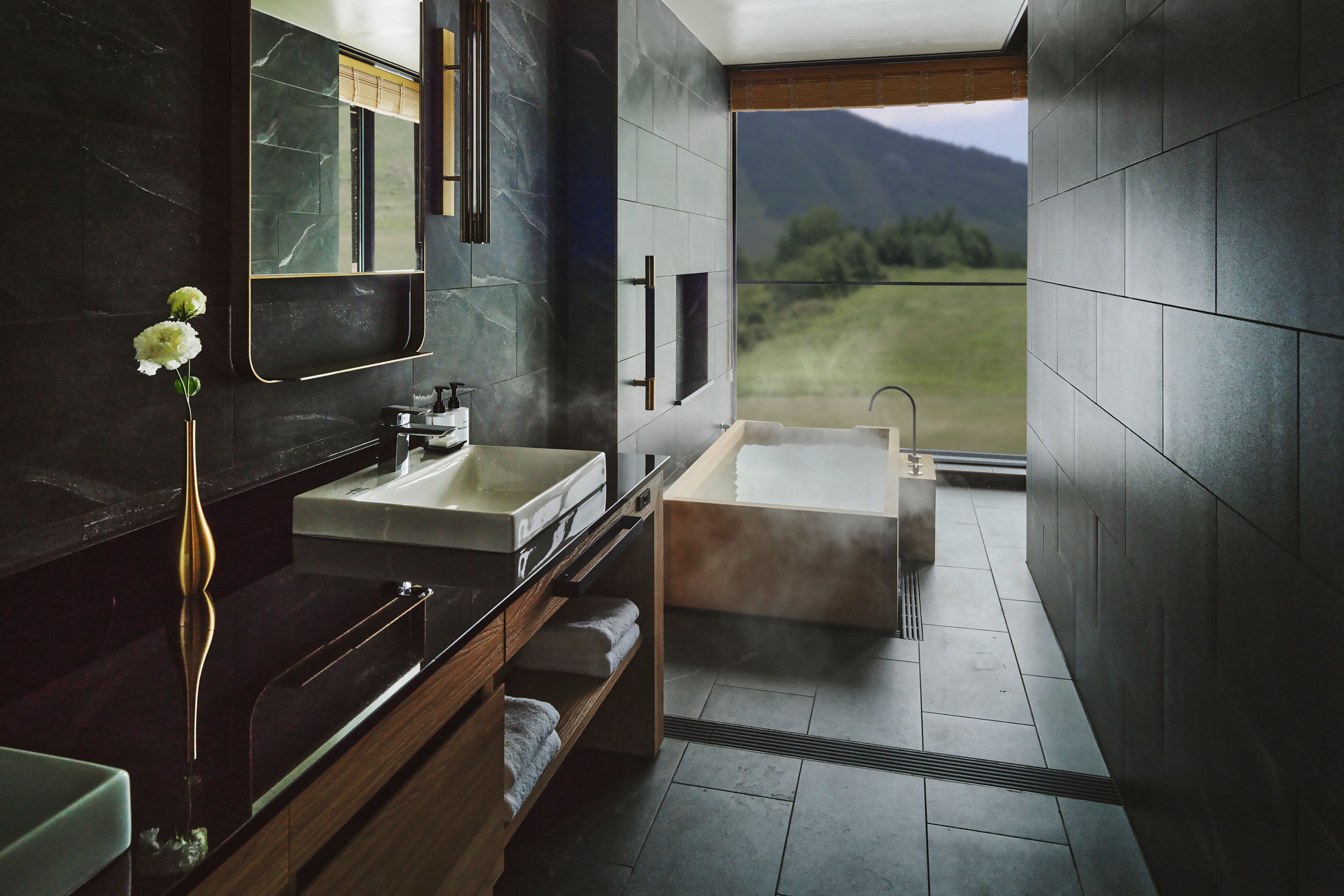 A modern bathroom with a large mirror, a sink, a bathtub, and a view of a mountainous landscape.