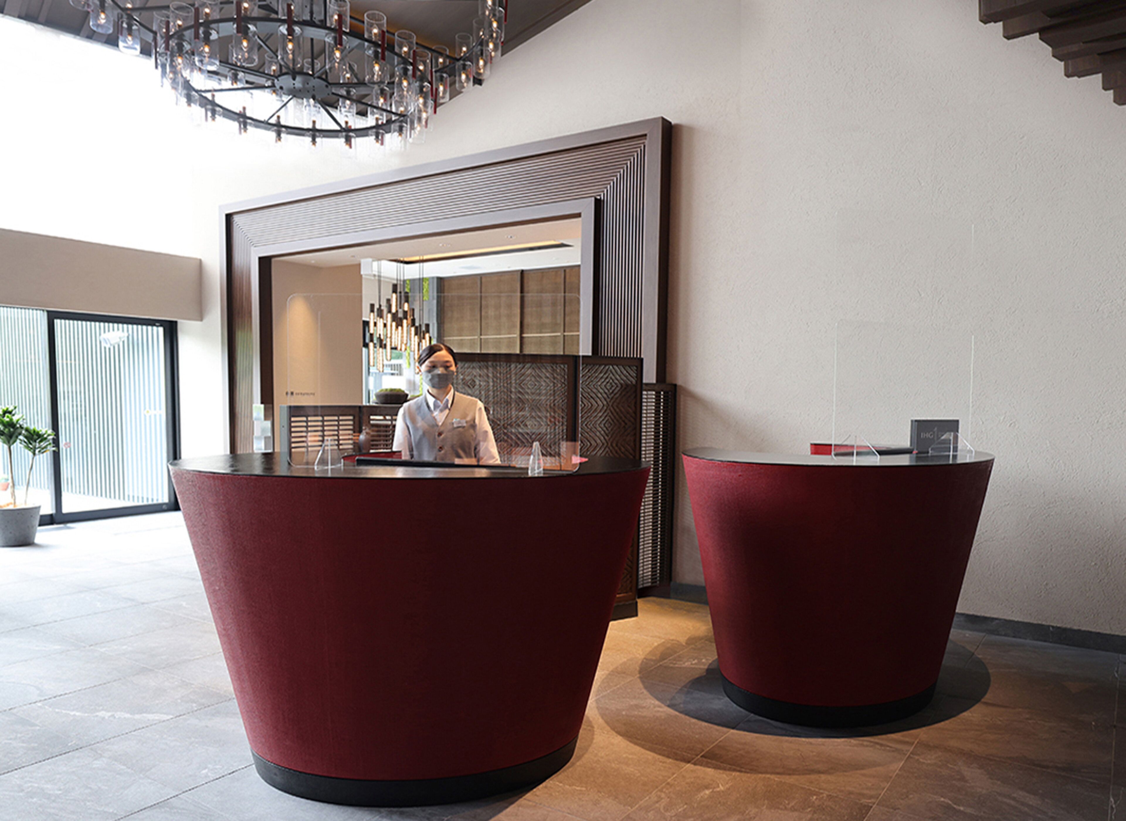 A reception area with two red reception desks, a modern chandelier, and a large window.
