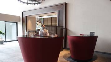 A reception area with two red reception desks, a modern chandelier, and a large window.