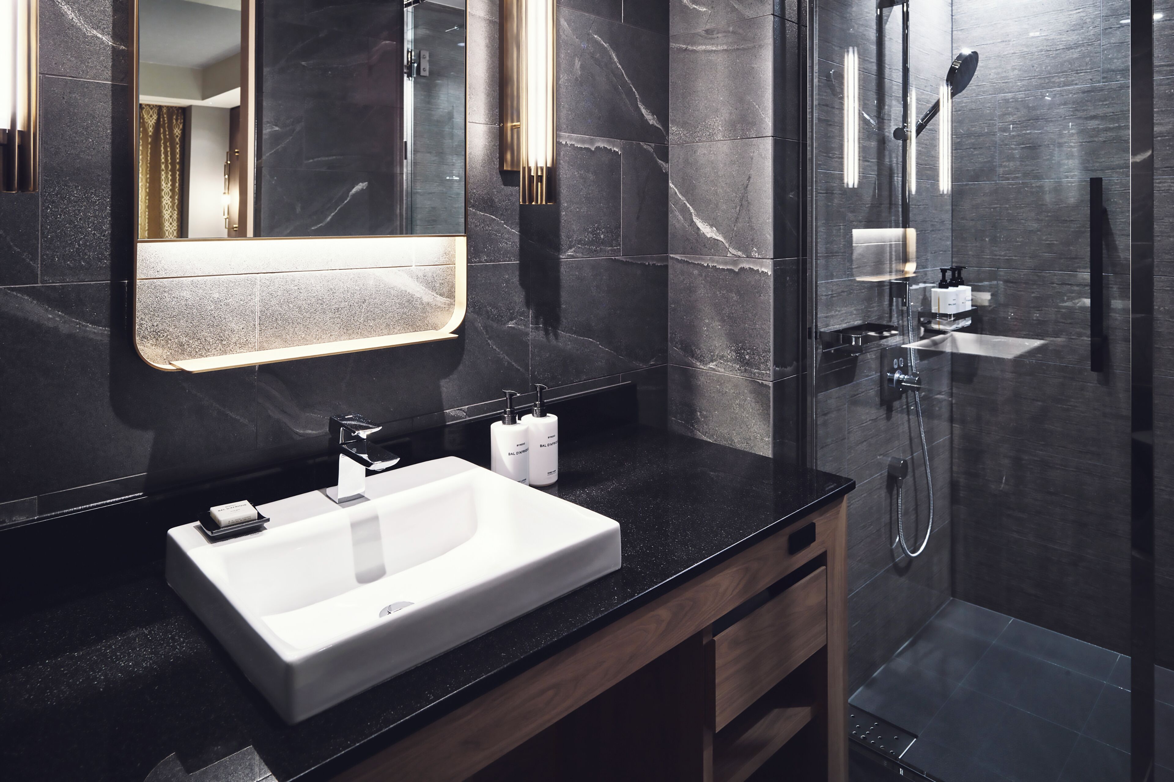 A modern bathroom with a large mirror, a white sink, and a glass-enclosed shower area.