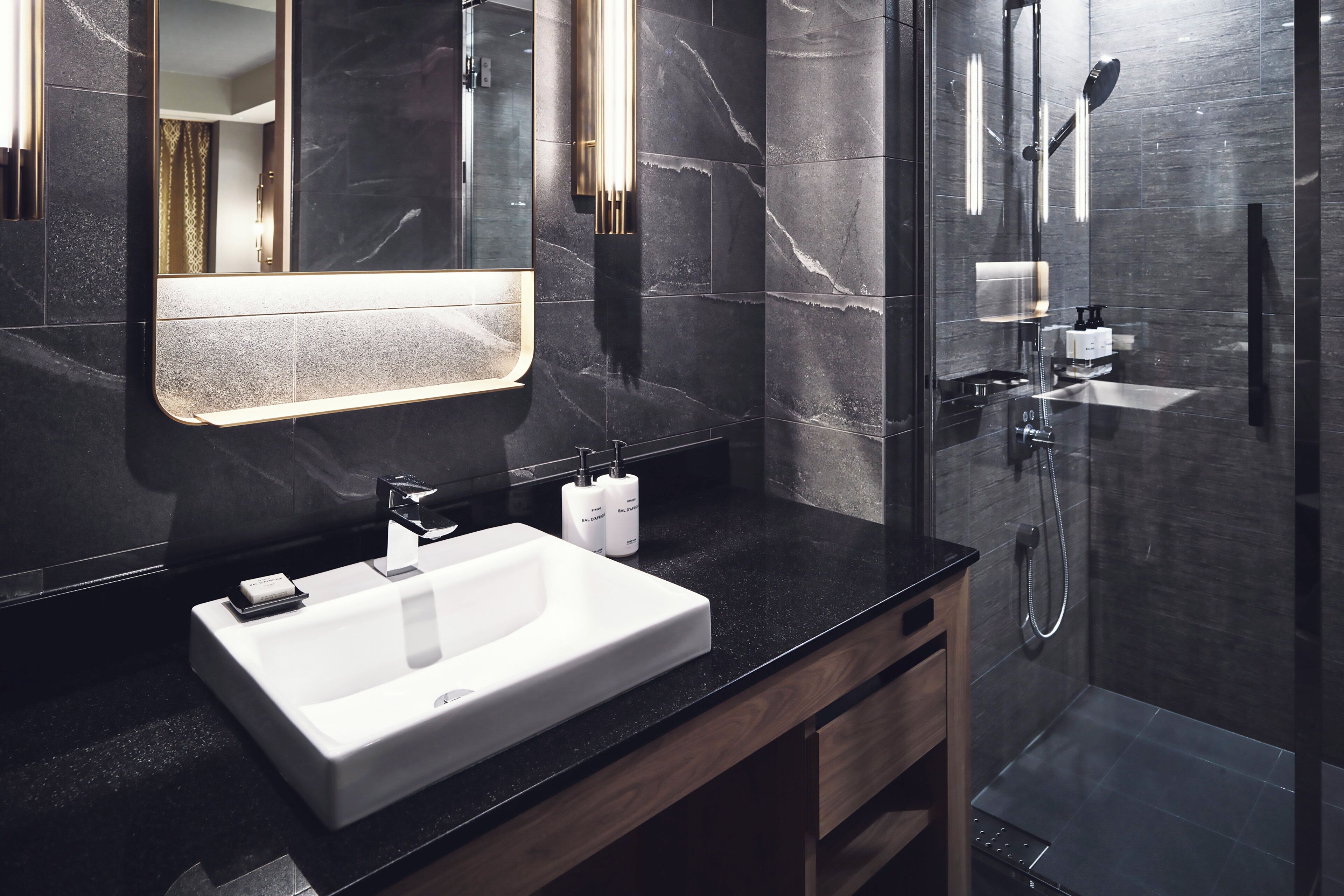 Une salle de bain moderne avec un grand miroir, un lavabo blanc et une douche séparée par une paroi de verre.