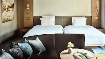 Habitación de hotel con cama doble, sofá, una pequeña mesa con un florero y un libro, y una lámpara de pared.