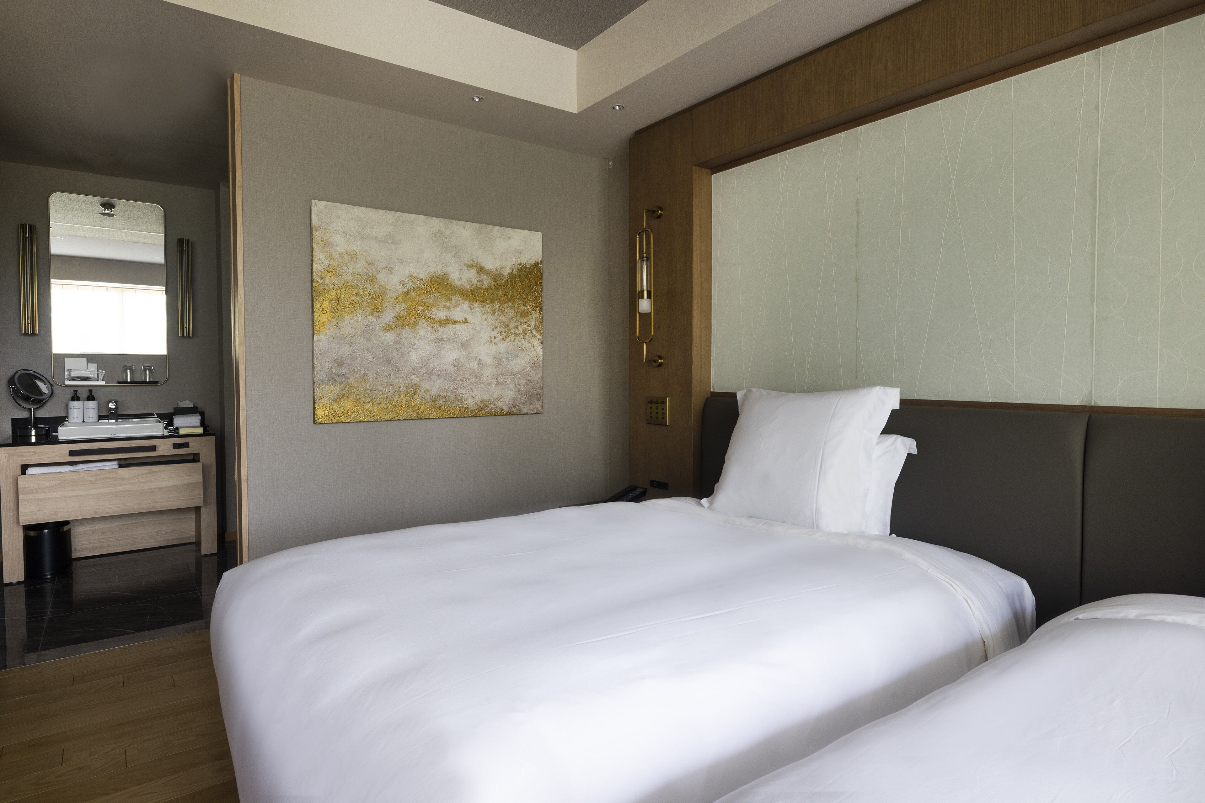 Habitación de hotel con dos camas, un escritorio con espejo y un cuadro abstracto grande en la pared.