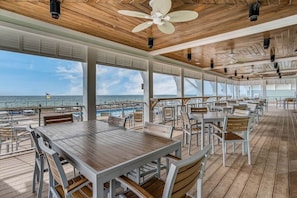 An outdoor dining area with tables and chairs, large windows, and a view of the ocean. - Paradise Found at Lost Key Resort: Tropical Bliss (Pensacola)