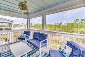 A covered porch with blue cushioned seating, a small table, and a ceiling fan.