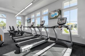 A gym with treadmills, exercise bikes, and a large window with a view of a park.