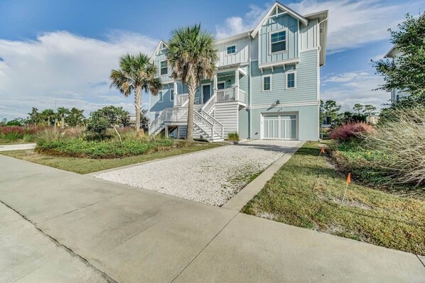 A multi-story building with a front entrance, a driveway, and a small garden area with palm trees.