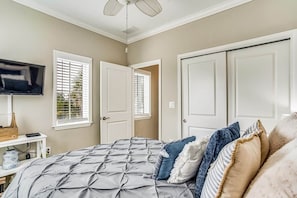 A bedroom with a bed, a TV, a desk, and a window with blinds.