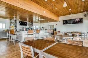 A restaurant with wooden tables and chairs, a bar area, and a large TV screen on the wall.