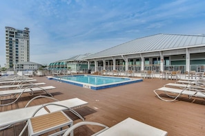 Un área de piscina con sillones reclinables, una piscina y un edificio con techo metálico.