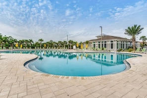 A swimming pool with lounge chairs and umbrellas, surrounded by palm trees and a building with a tiled roof.