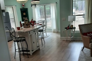 Una cocina con isla central, taburetes de bar, refrigerador y mesa de comedor.