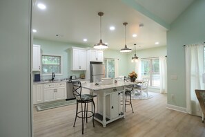 A spacious kitchen with white cabinets, a central island with bar stools, pendant lighting, and large windows. - Hope House - Christian Retreat (Eastman)