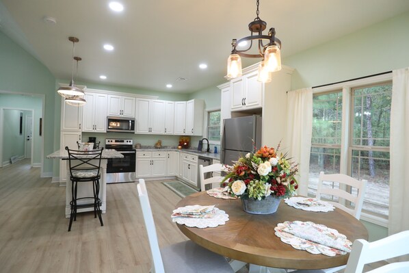 A spacious kitchen with white cabinets, a central island, and a dining area with a wooden table and chairs. - Hope House - Christian Retreat (Eastman)
