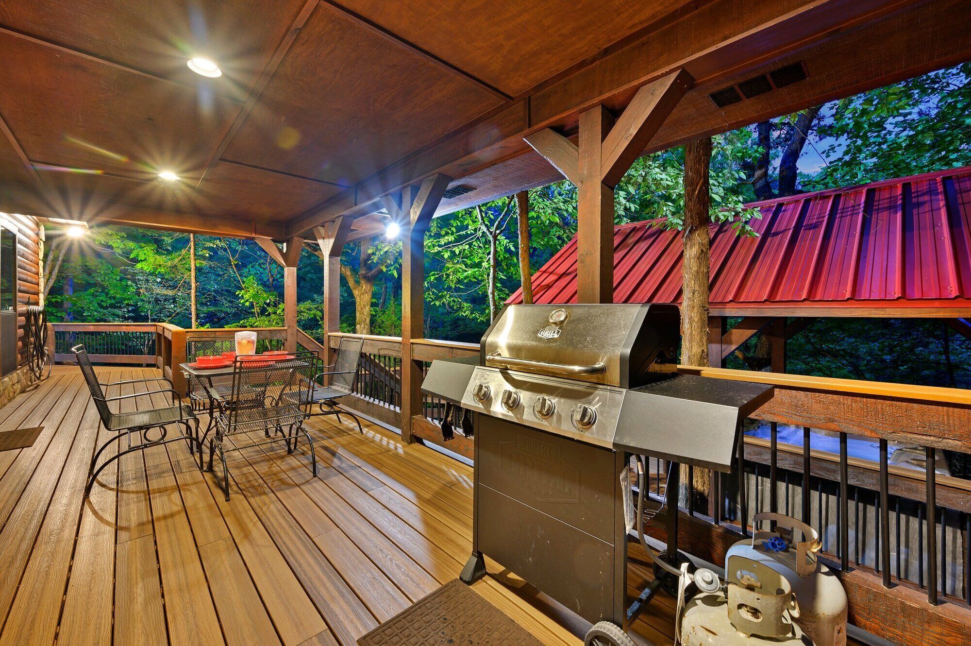 Een terras buiten met een barbecue, houten meubilair en uitzicht op het bos.