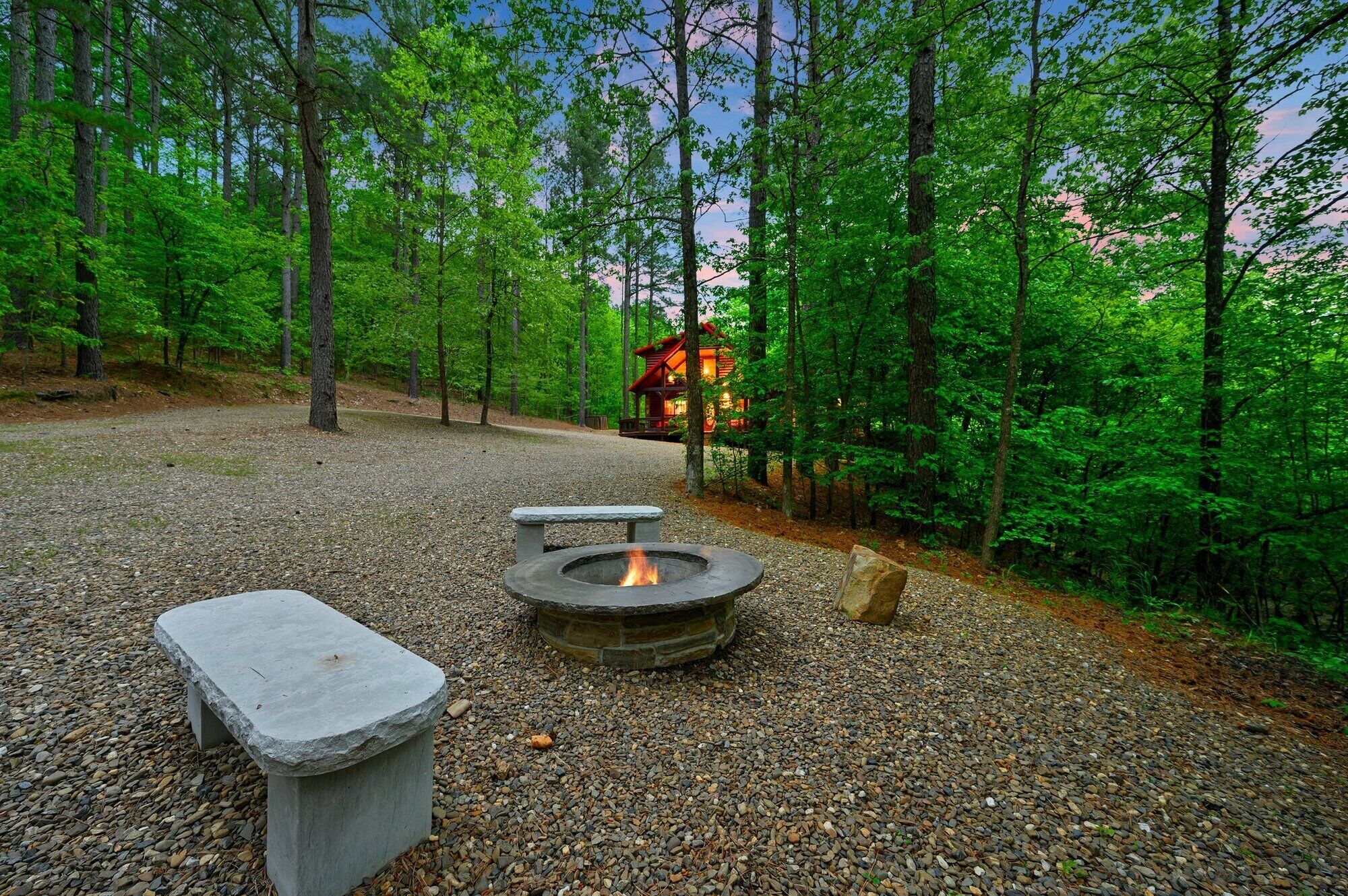 A forested campsite with a stone fire pit and seating area.