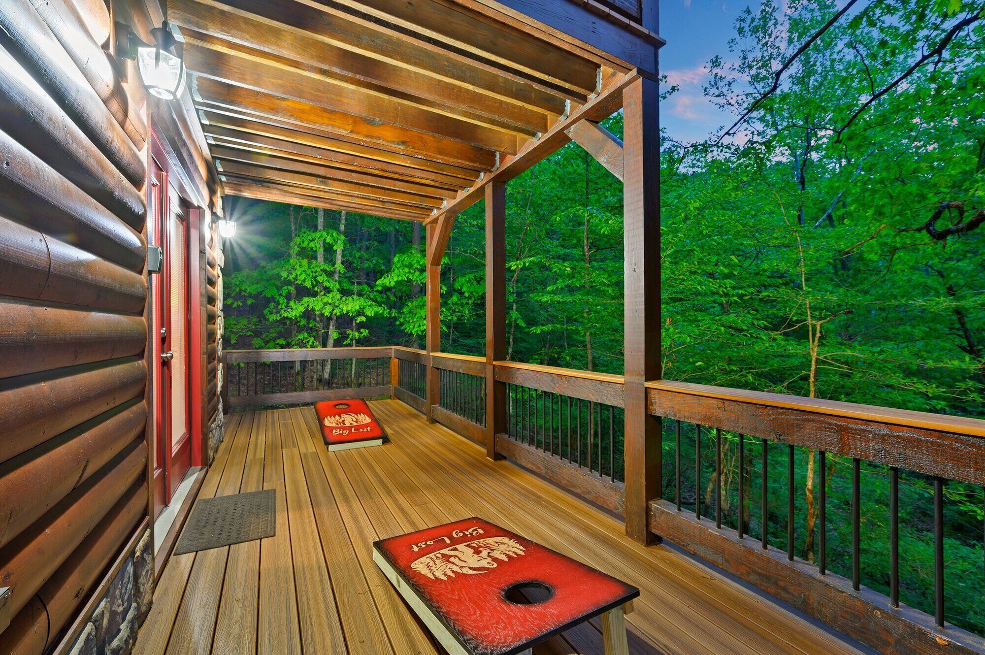 A wooden deck with two red bean bag chairs, a wooden railing, and a view of a forested area.