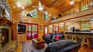 Ein Blockhaus-Interieur mit Kamin, einer schwarzen Ledersofa, einem Essbereich und einer Küche.