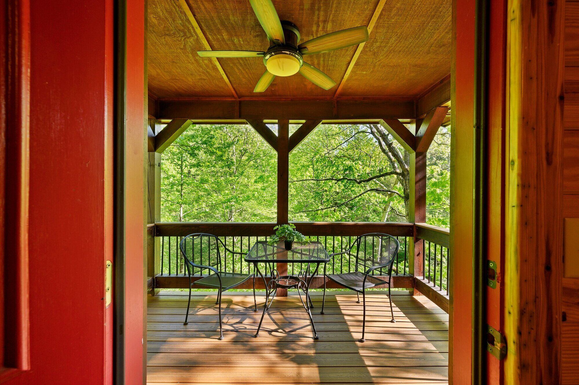 Uma área externa coberta com ventilador de teto, deck de madeira e mesas e cadeiras de metal.
