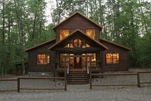 A log cabin with a front porch, stone foundation, and a gravel driveway.
