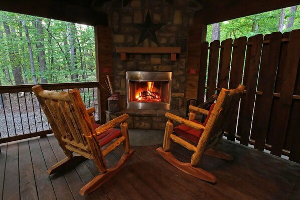 A cozy wooden deck with two rocking chairs facing a stone fireplace.