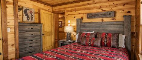A wooden cabin bedroom with a bed, dresser, and a ceiling fan.