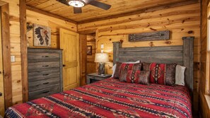 Une chambre dans une cabane en bois, avec un lit, une commode et un ventilateur de plafond.